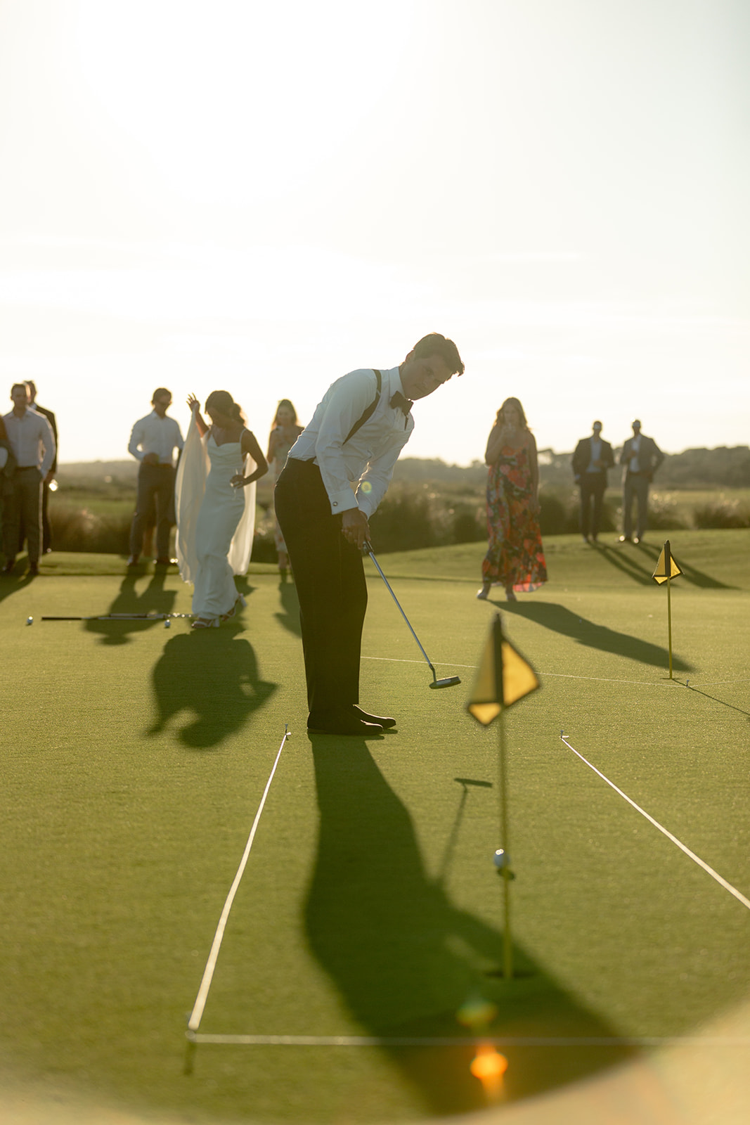 Groom is putting with wedding guest in background watching
