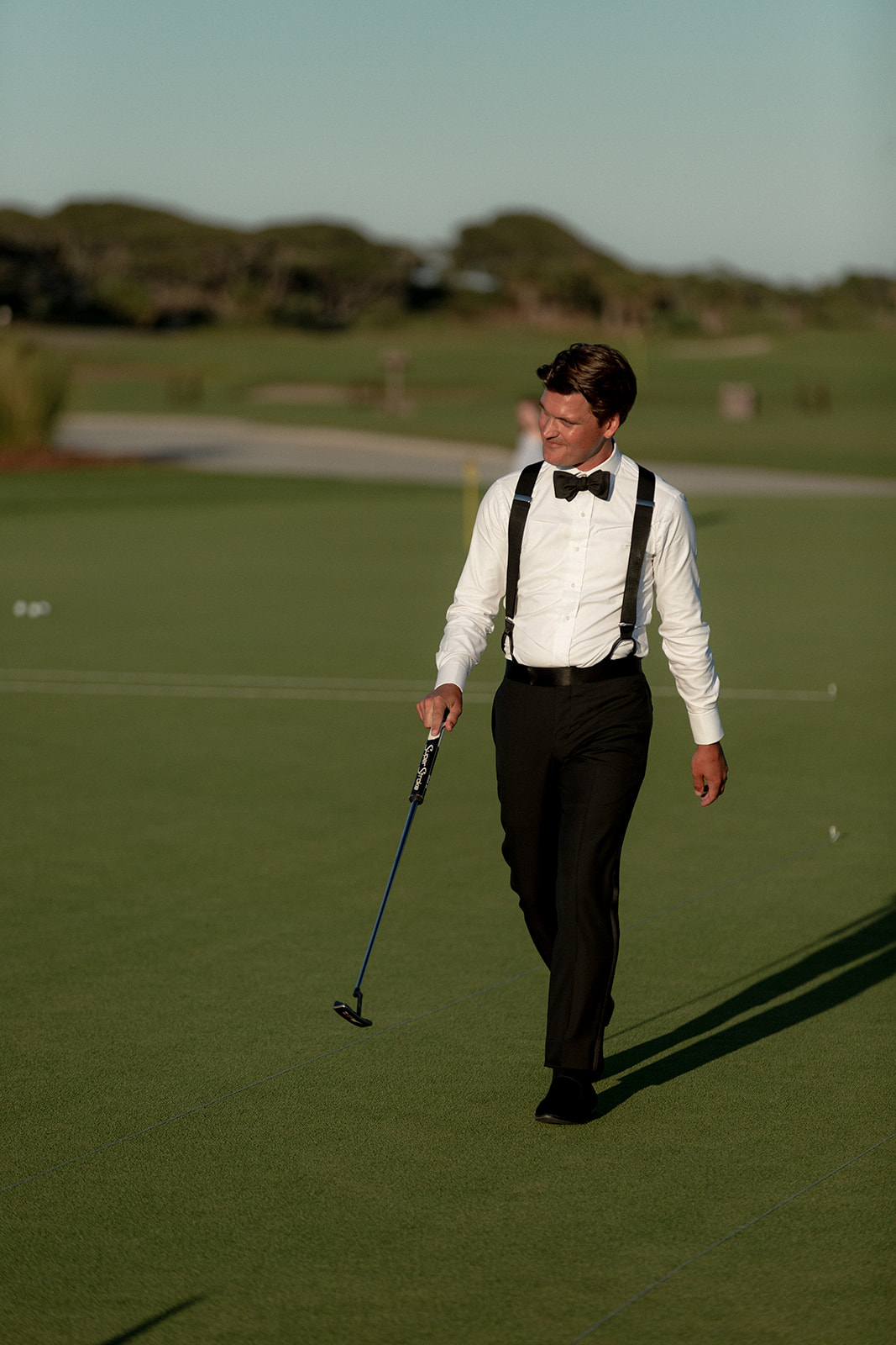 Groom walking with putter over green at Kiawah Ocean Course wedding