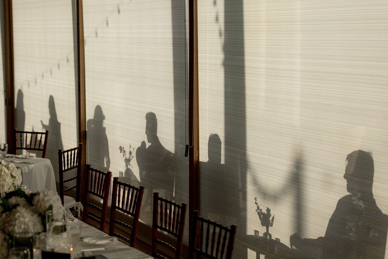 Shadows of wedding guest on blinds photographed from inside during cocktal hour.