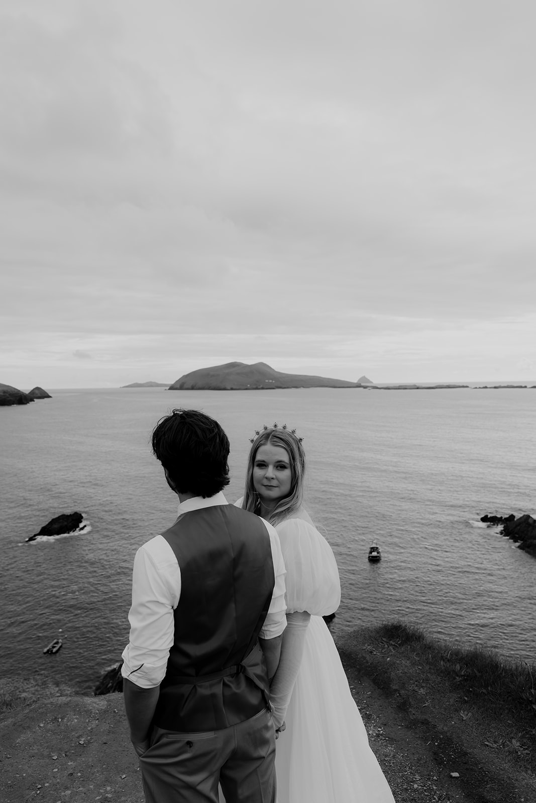 Black and white photo of bride and groom standing at irish cliffs with ocean in the background
