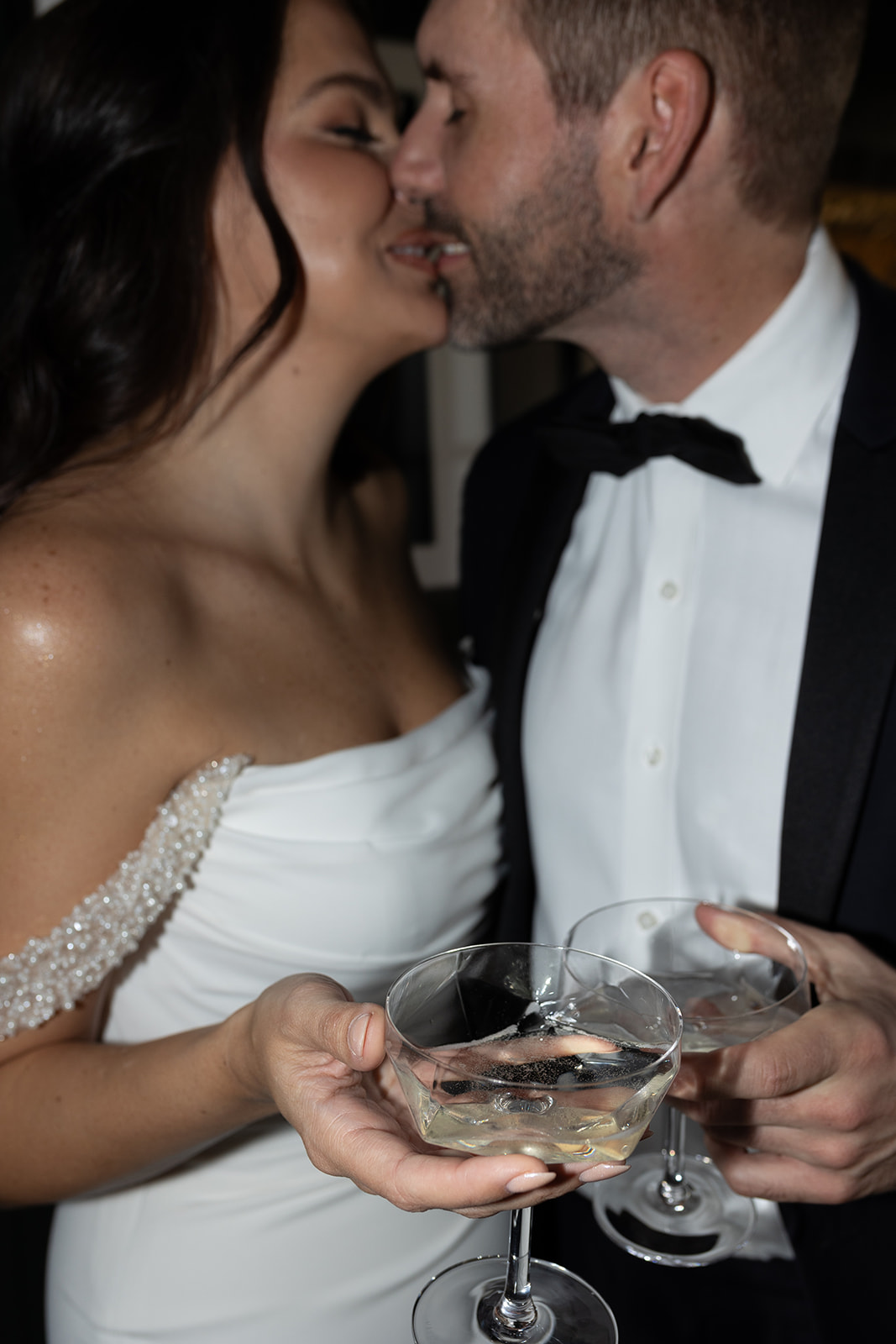 Bride and groom kiss while holding cocktail glasses in their hand