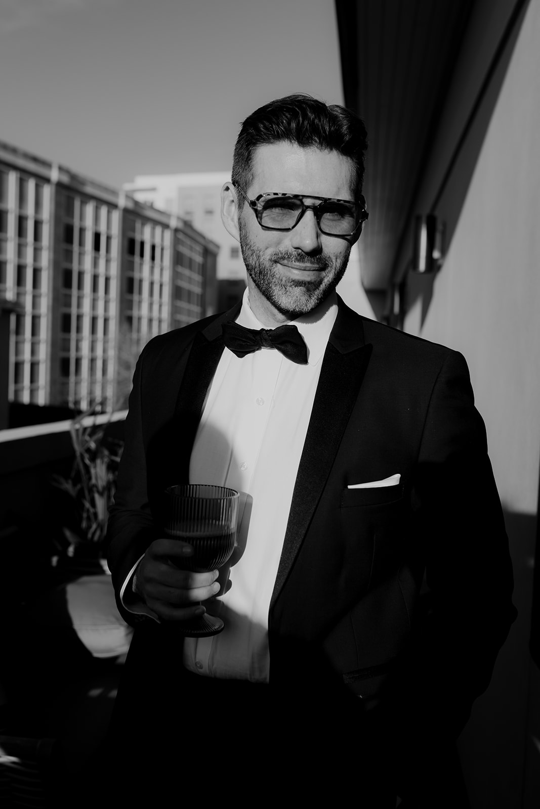 Black and white photo of groom with sunglasses standing on balcony