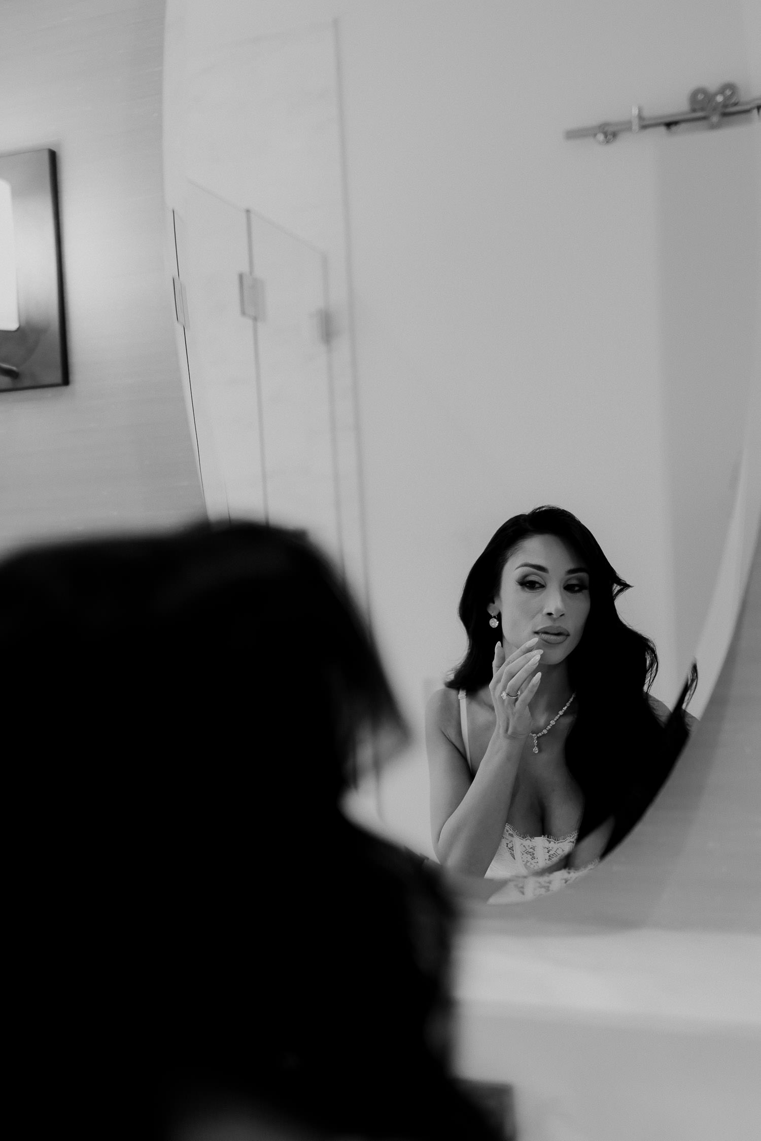 Black and white photo of Bride loking into mirror dyring getting ready