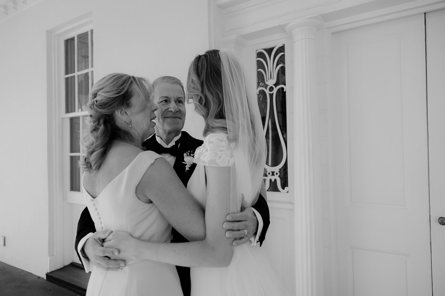 Black and white photo taken at Charleston wedding. Bride, mosther and father of bride hug each other.