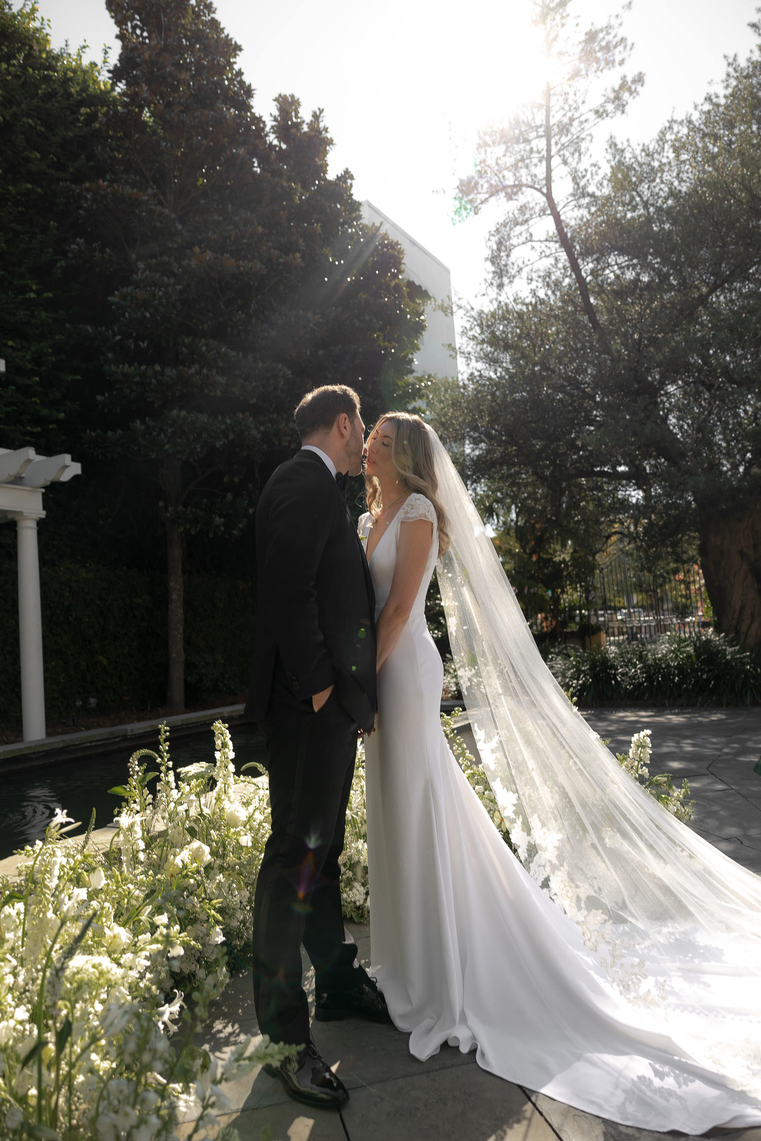 couple portraits taken outside with sun shining from the back and florals on the ground