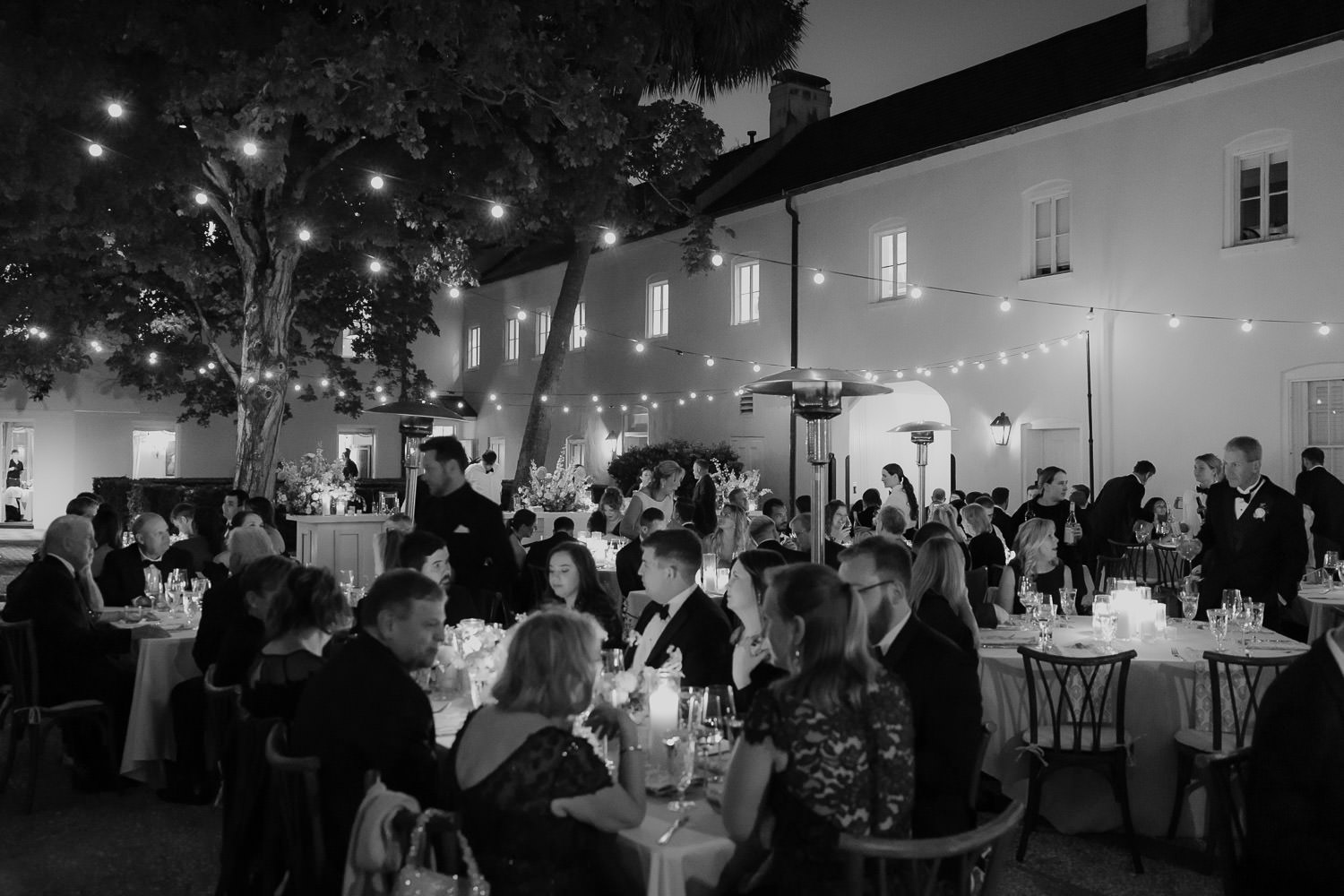 Black and white photo of guest seated at wedding recptionenjoying charleston wedding celebration outdoor.