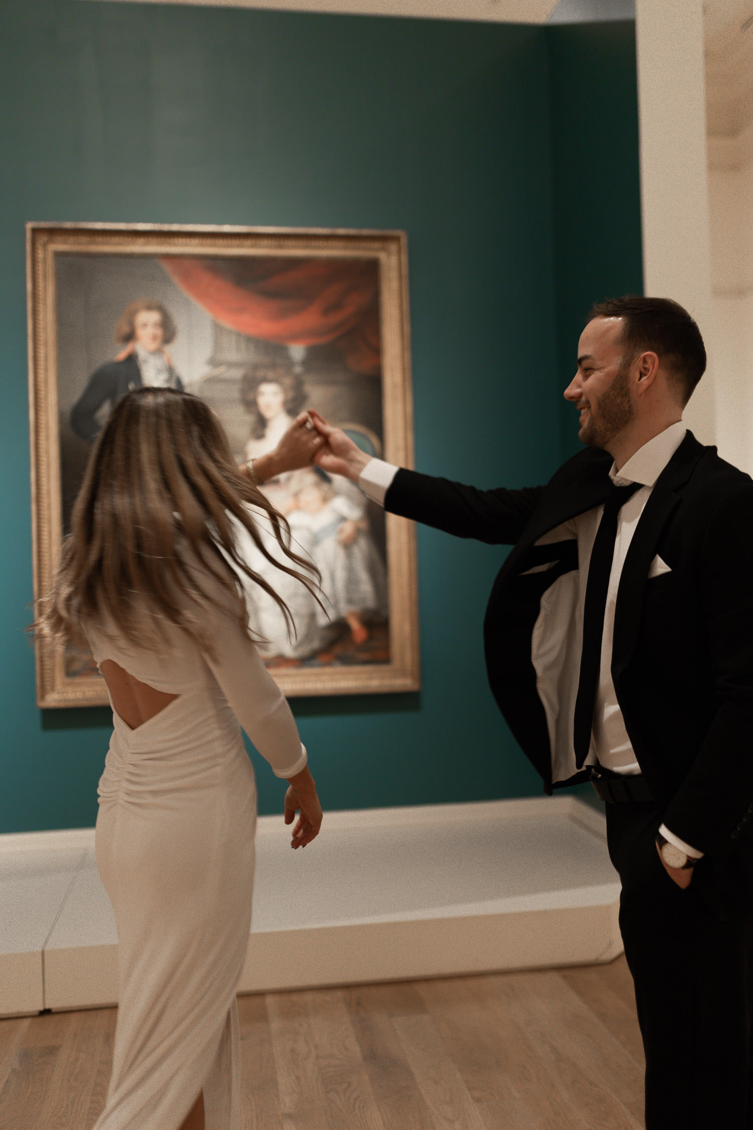 Couple enjoying time at the museum. Man twirling woman with painting in the background