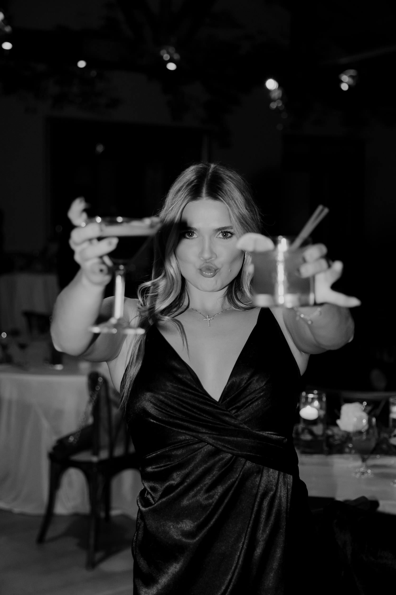 Black and white photo of wedding guest showing cocktails into the camera.