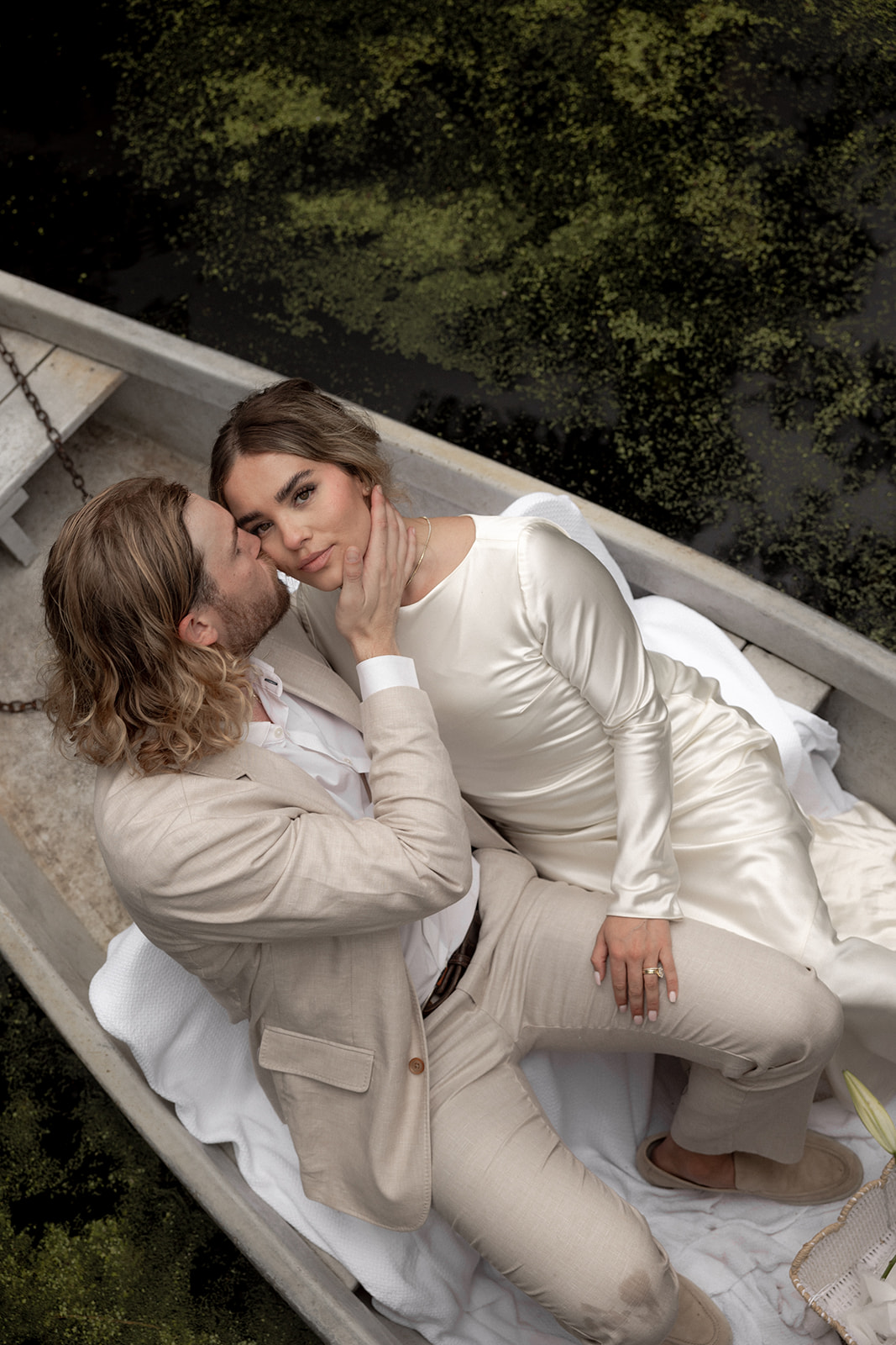 Couple in iconic boat at Cypress Gardens. Groom kisses bride on the while she looks at the camera. Cypress Gardens Elopement