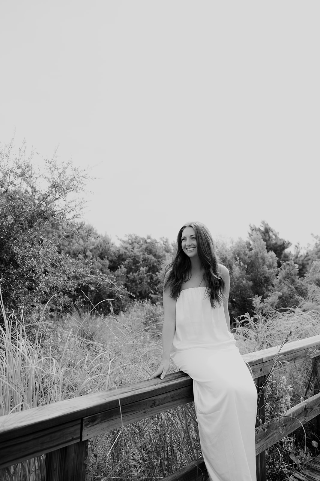 Woman sitting on wooden reiling with greenery in background