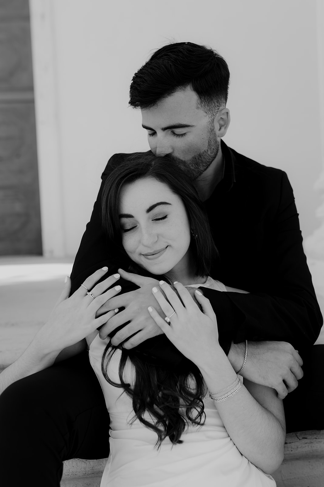 Engaged couple sitting. Her between his legs while he kisser her on the back of her head