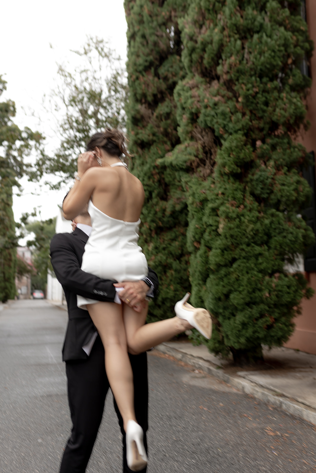 Man in black suit lifting up fiance in white neckholder dress and twirling her. Great Engagement Look