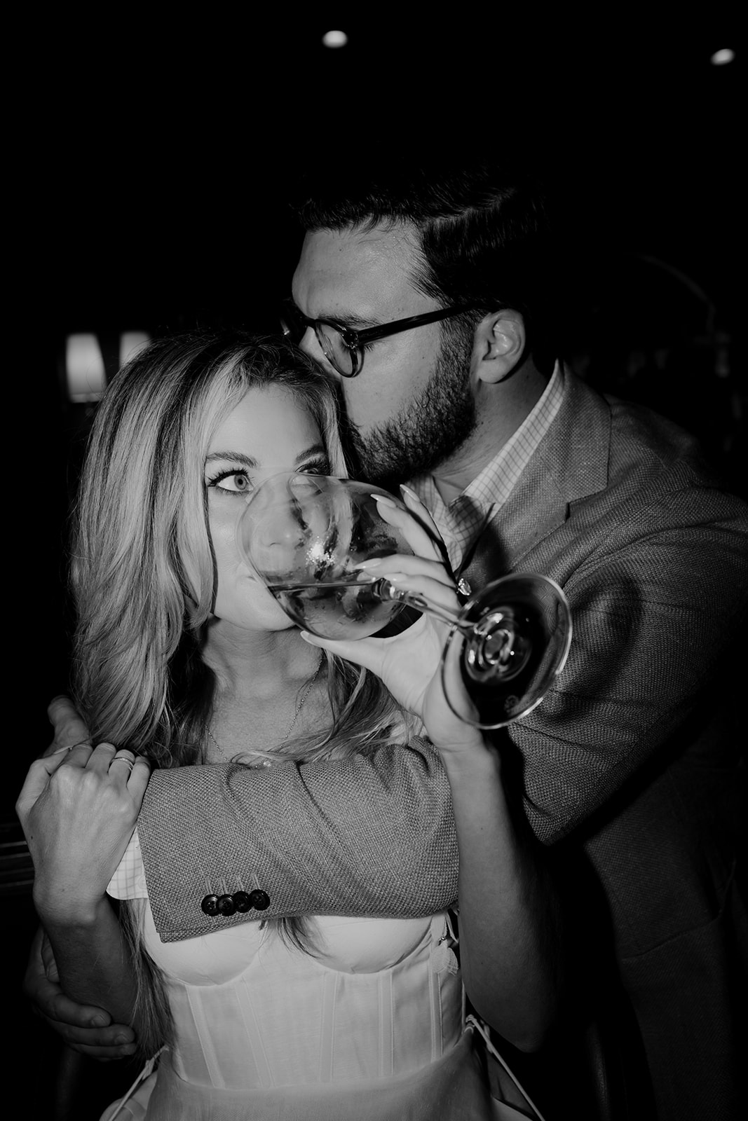 black and white photo taken at Downtown Engagement session. Woman drinking wine while man has arm wrapped around her chest. The Palmetto Lobby Bar