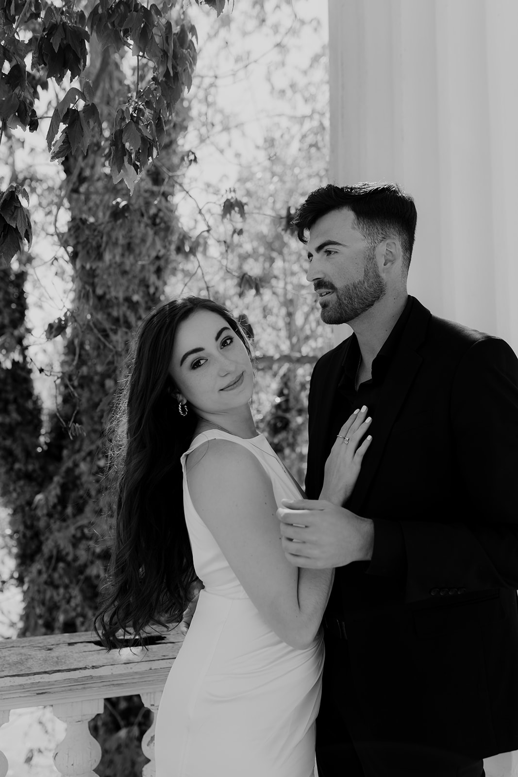 black and white photo. Couple in black and white engagement attire. He is looking to the side and she looks straight into the camera