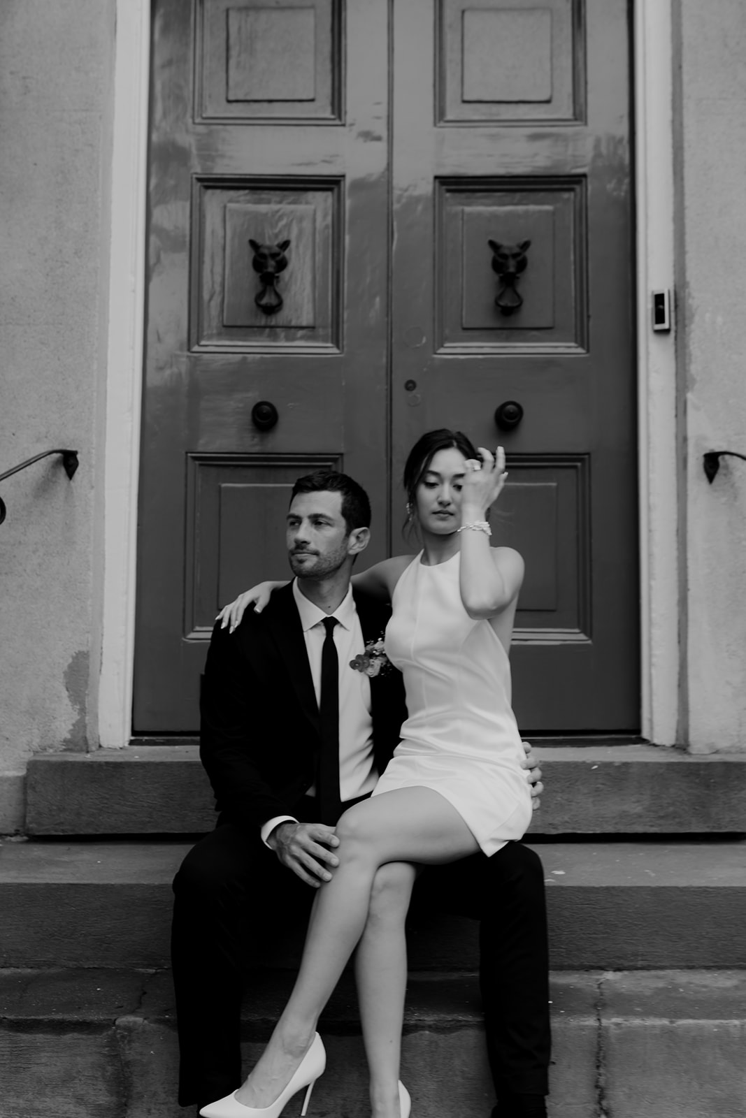 Woman in white neckholder dress sitting on mans lap. Charleston door in background. Stunning Engagement Look for photo session