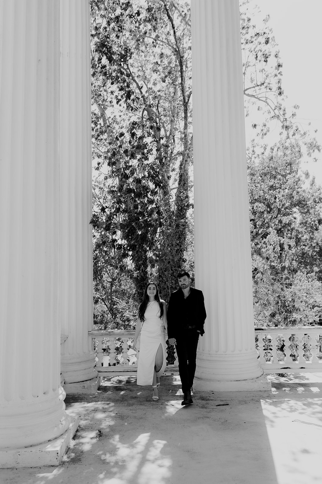 Couple walking towards camera with high greek columns in background. Captured in black and white