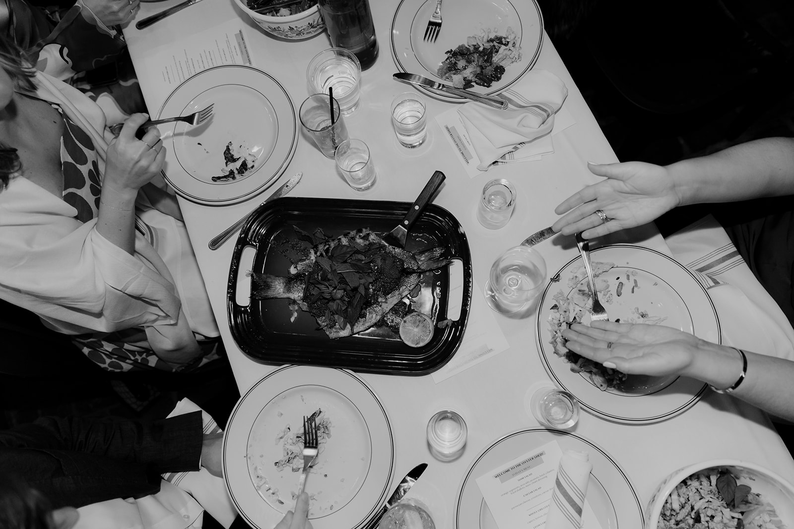 Family style dinner served at Rehearsal Dinner at Leon's Oyster Shed. PLates with food on table photographed in black and white