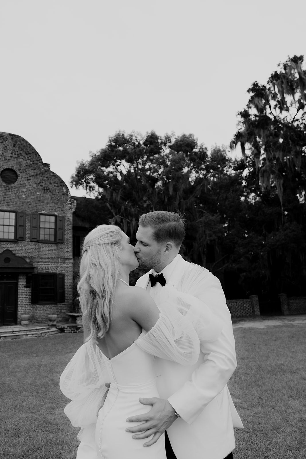 Bride and groom kissing in front of the Middle Place house photographed in black and white