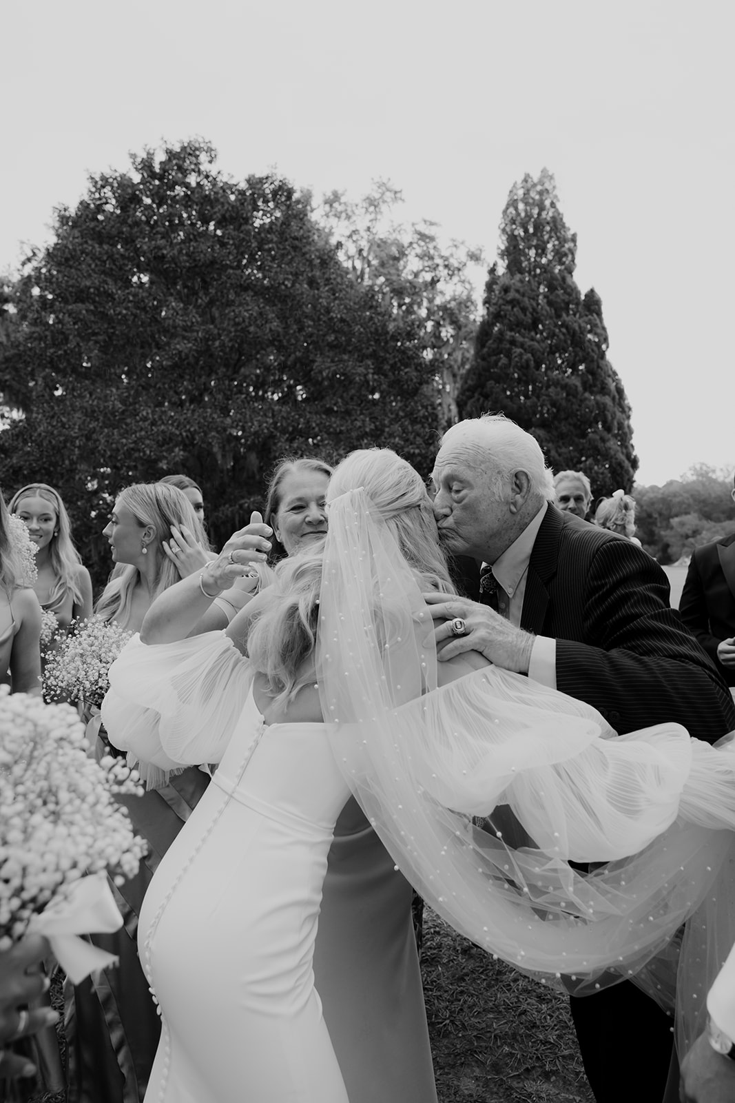 Bride is congratulated by grandfather after ceremony, captured in timeless black and white