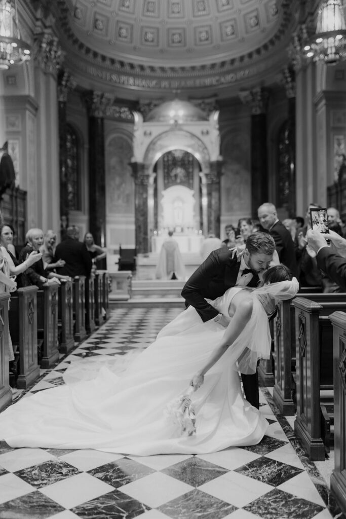 Groom is dipping his wife in the middle of the aisle of  The Cathedral Basilica of Saints Peter and Paul. photographed in black and white