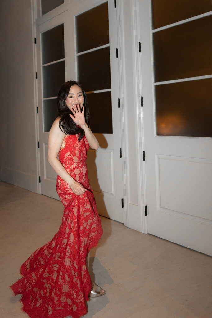 Bride in traditional chinese red dress at wedding in charleston. She is waving into the camera.